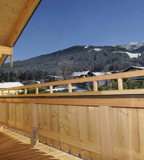 Balkon aus Holz mit Ausblick auf verschneite Alpenlandschaft und Häuser.